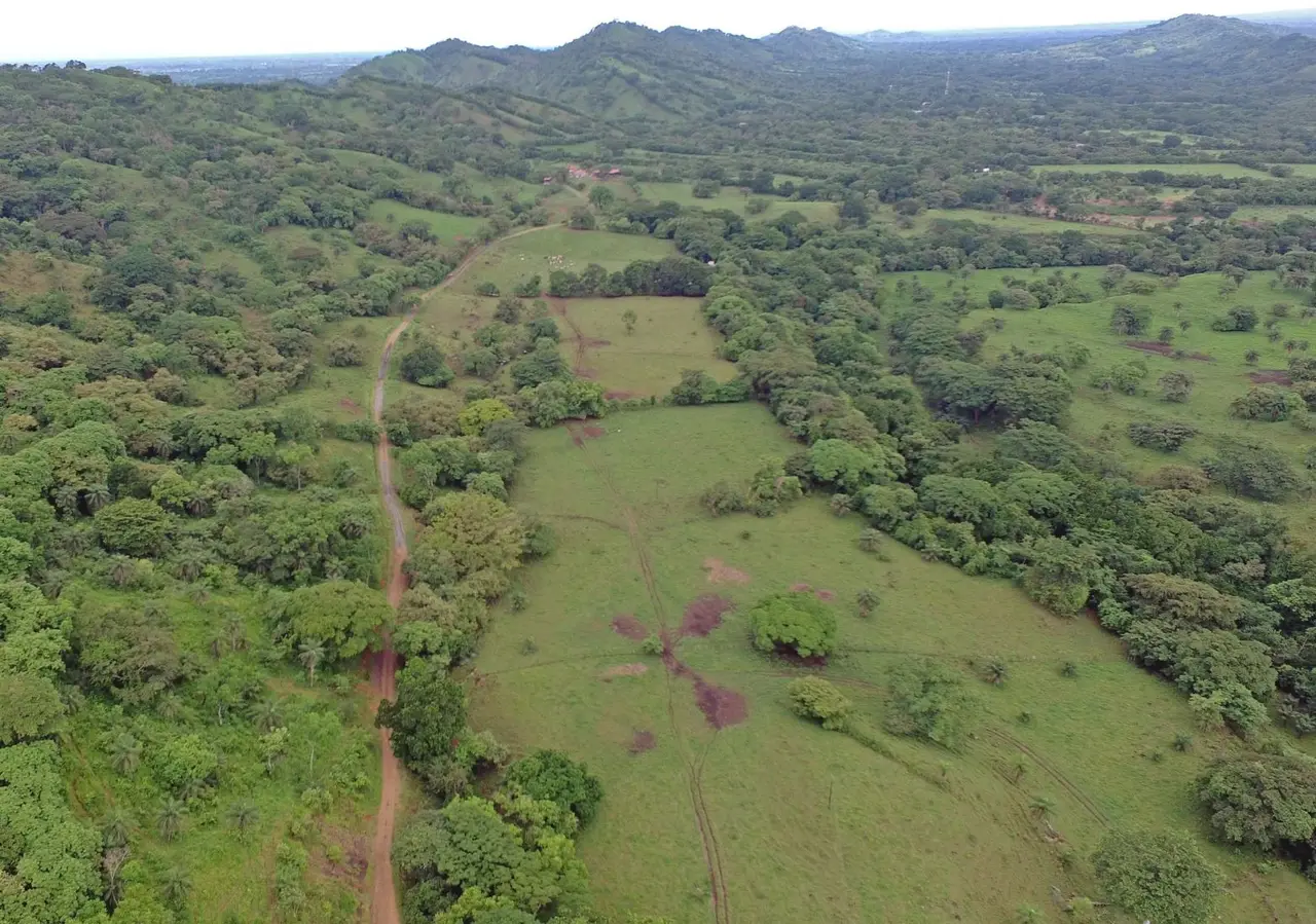 Vista aérea de la finca de Valleluna antes de intervenir: potreros ondulados, un camino de tierra y cerros boscosos al fondo.